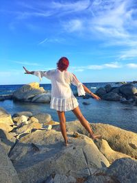 Rear view of man standing on rock at beach against sky