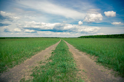 Dirt road amidst field against sky