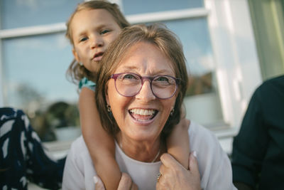 Happy senior woman piggybacking granddaughter at porch