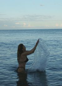 Woman in sea against sky during sunset