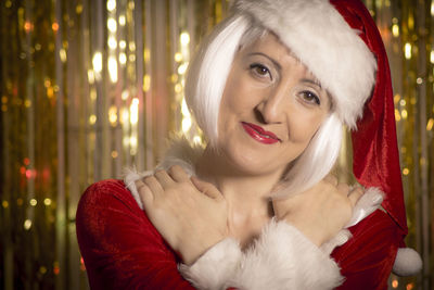 Portrait of smiling mature woman wearing santa hat while standing at home