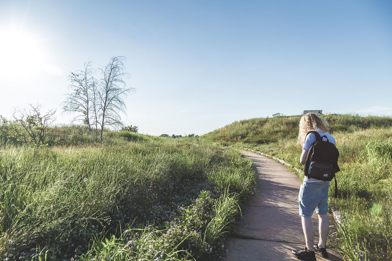 REAR VIEW OF WOMAN WALKING ON GRASSY FIELD