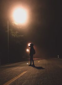 Side view of silhouette man walking on road at night
