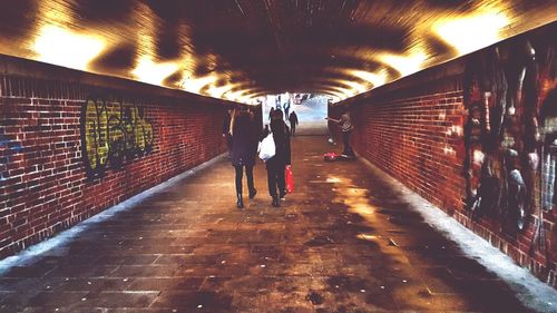 Rear view of people walking on illuminated tunnel