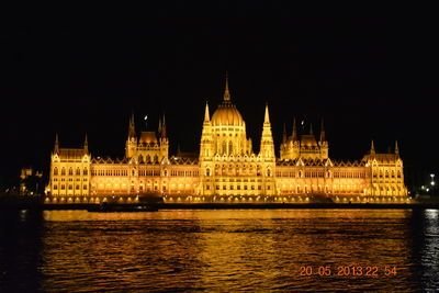 Illuminated hungarian parliament building by danube river against sky at night