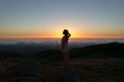 Young woman standing on landscape against sky during sunset