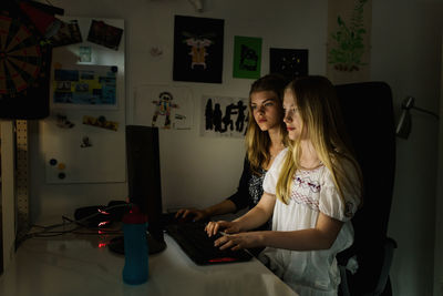 Teenage girls using computer in darkroom at home