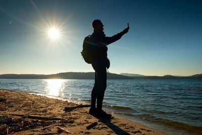 Man standing at beach against sky during sunset