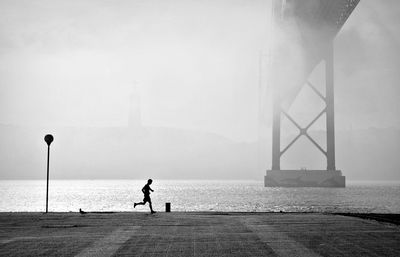 Side view of silhouette boy running on footpath by river during foggy weather