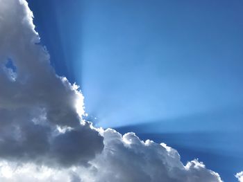 Low angle view of sunlight streaming through clouds