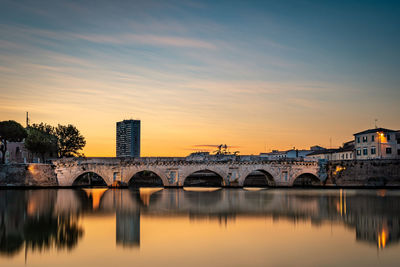 Arch bridge over river against sky during sunset