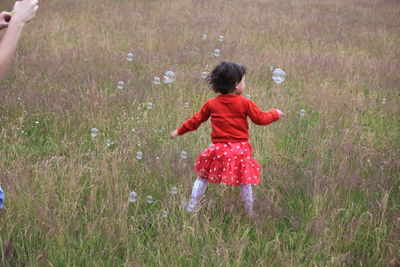 Rear view of girl playing with bubbles on grassy field
