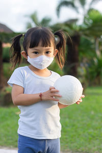 Portrait of cute girl wearing mask holding ball at playground