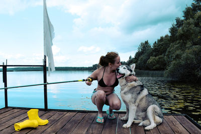 Woman with husky dog sitting on a pier against the sky