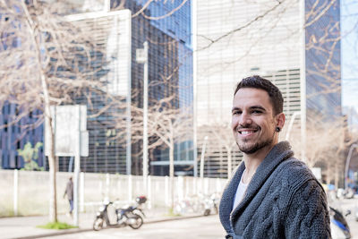 Smiling bearded young man standing against office buildings