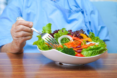 Midsection of person holding fruits in bowl on table