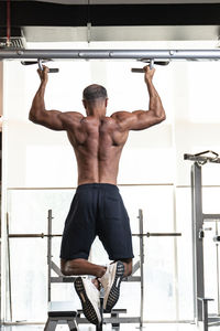 Rear view of shirtless man exercising in gym