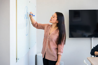 Smiling confident businesswoman drawing diagram on whiteboard in meeting room at office