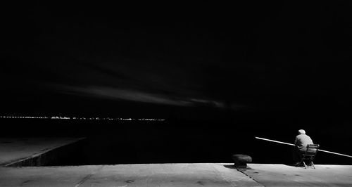 Man standing by retaining wall against sea at night