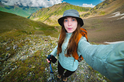 Young woman taking selfie portrait hiking mountains - happy hiker on the top of the cliff smiling at