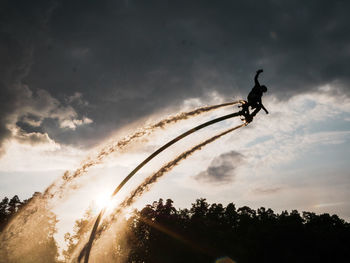 Low angle view of silhouette man flyboarding against cloudy sky at sunset