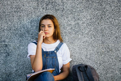 Portrait of a beautiful young woman sitting against wall