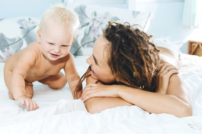 Mother playing with shirtless daughter while lying on bed at home