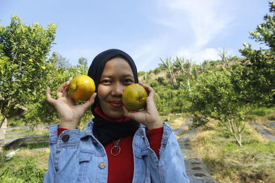 Portrait of young woman holding oranges at farm