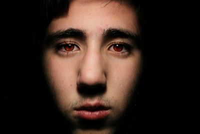 Close-up portrait of man with red eyes against black background