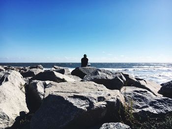 Man on rock by sea against clear sky