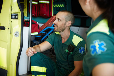 Male paramedic discussing with coworker while sitting in ambulance in parking lot