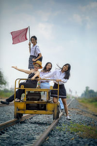 People sitting on vehicle on railroad track against sky