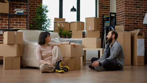 Woman sitting by boxes talking with man at home