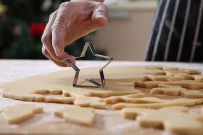 Cropped hands of chef cutting dough with pastry cutter at table