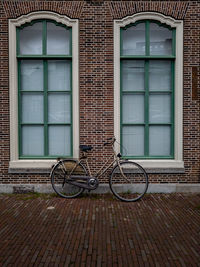 Bicycle between two windows and red brick wall