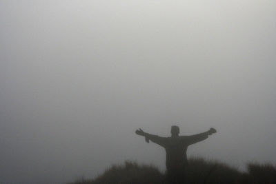 Silhouette man with arms outstretched standing against sky