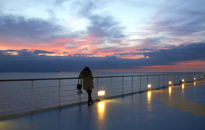Silhouette man standing by railing against sea during sunset