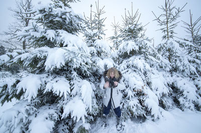 Mature woman standing on snow covered field against trees in forest