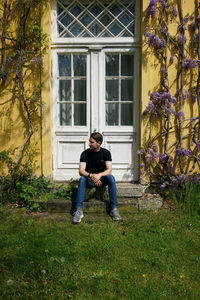 Full length of young man sitting on plant against building