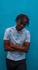 Young man looking away while standing against blue wall