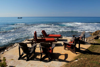 Chairs and table by sea against clear sky