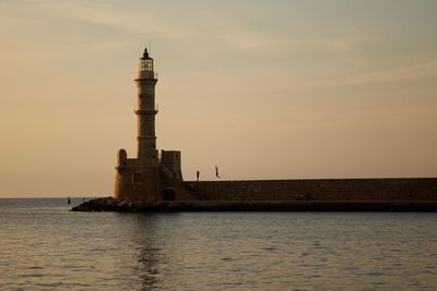 Lighthouse by sea at sunset