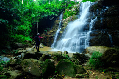 Man standing on rock against waterfall in forest