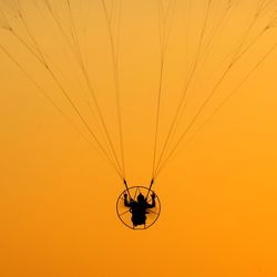 Low angle view of man cycling against orange sky