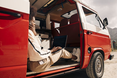 Woman using laptop and talking on smart phone while sitting in van during vacation