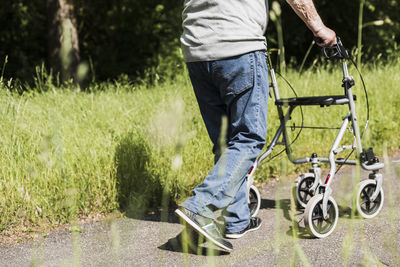 Back view of senior man strolling with wheeled walker in nature