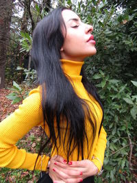 Young woman looking away while standing against plants