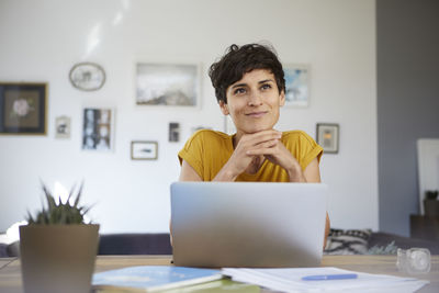 Portrait of smiling woman at home sitting at table using laptop