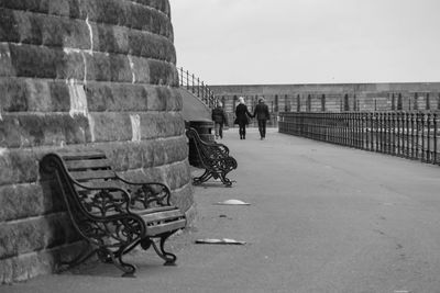 Empty bench by stone wall at walkway