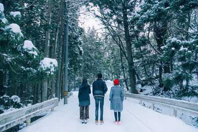 Rear view of friends standing on snow covered road in forest during winter